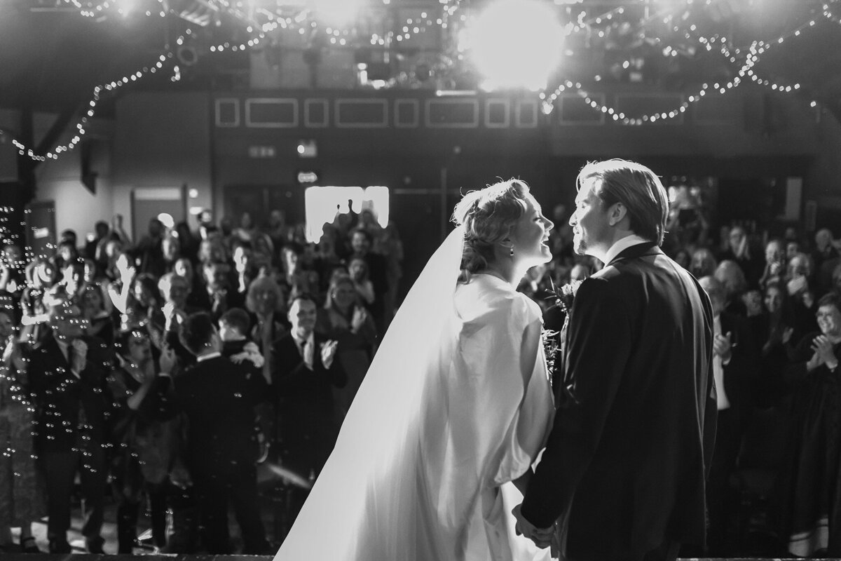 bride and groom on stage at a theatre wedding about to kiss you can see the audience behind them