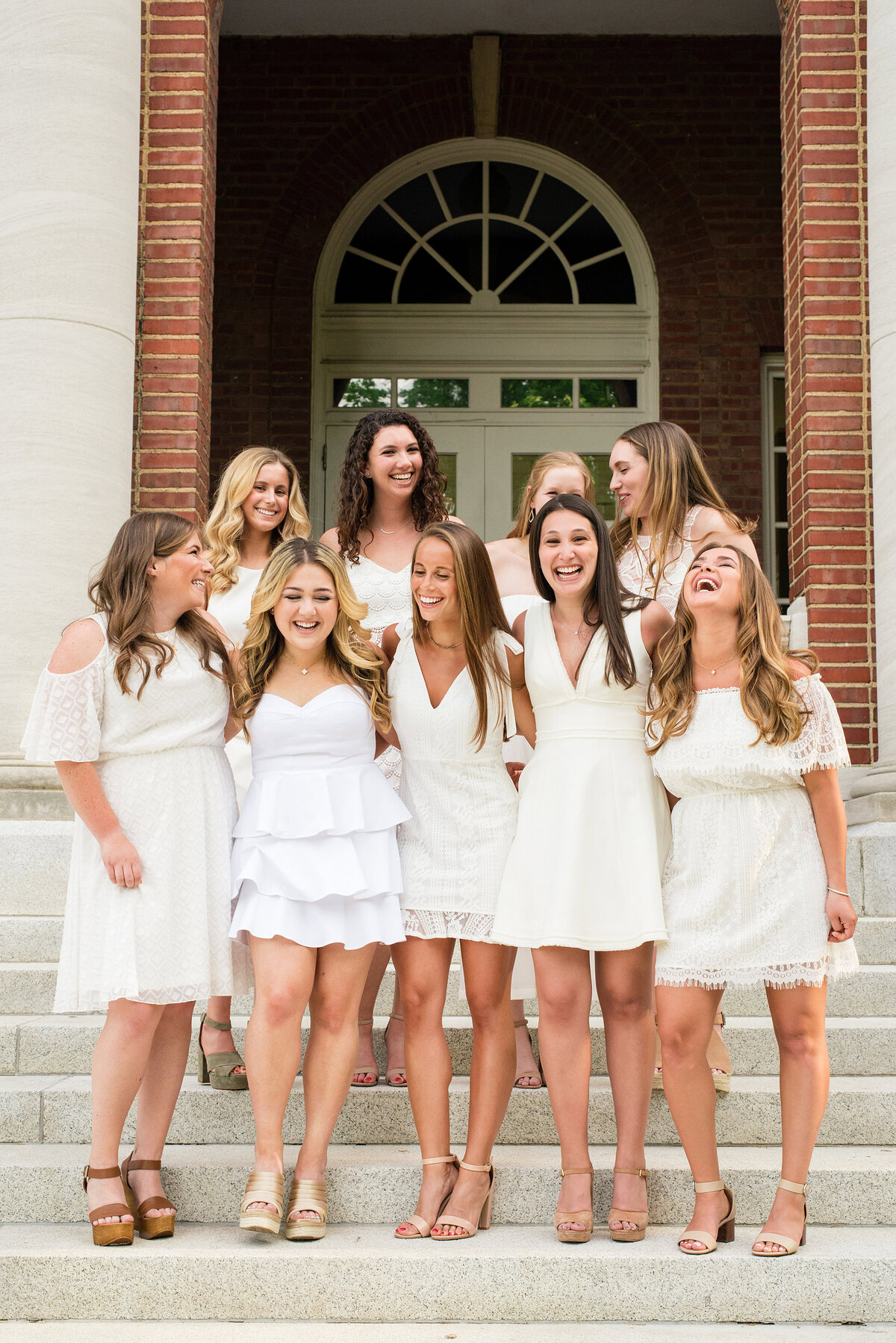 10 Senior girls on the steps at Vanderbilt University all wearing white dresses and laughing together