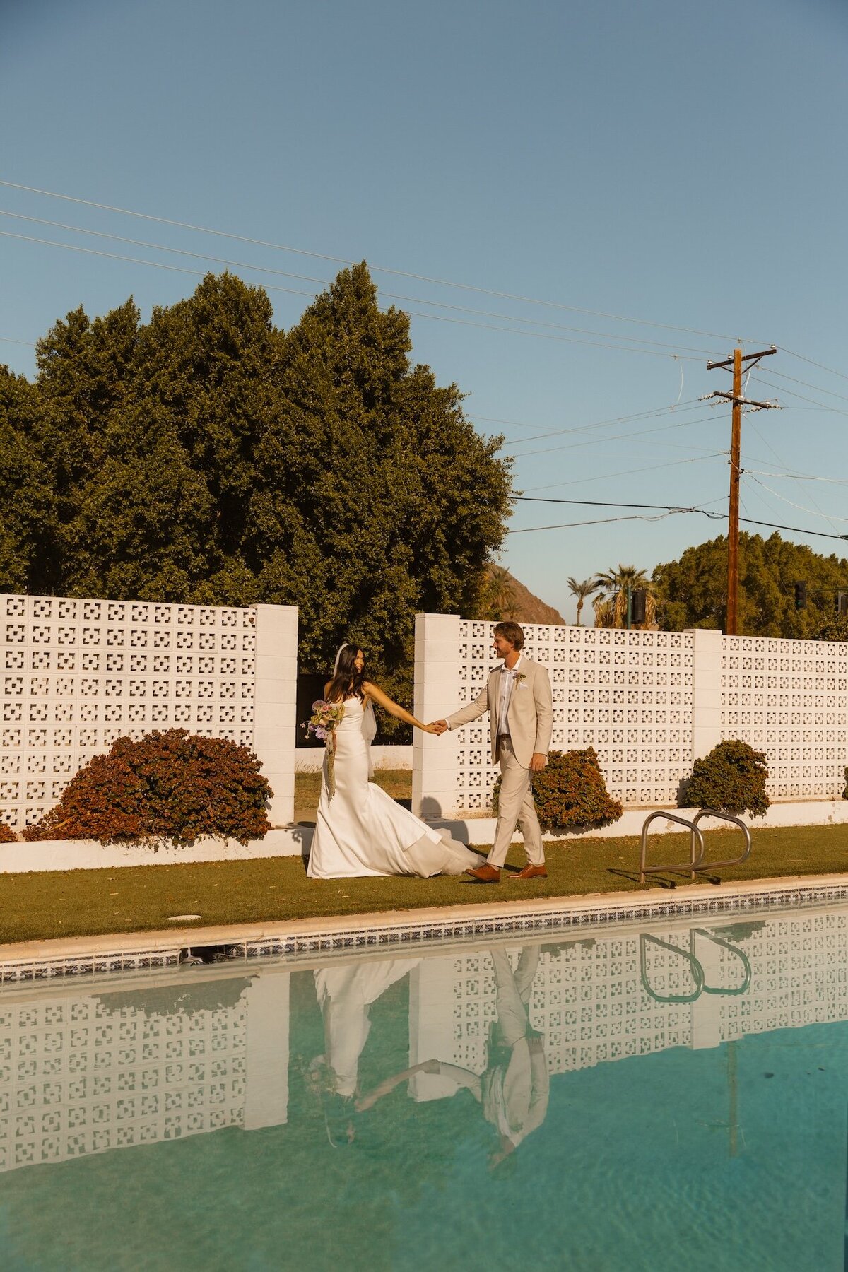 bride and groom hold hands next to pool in arizona