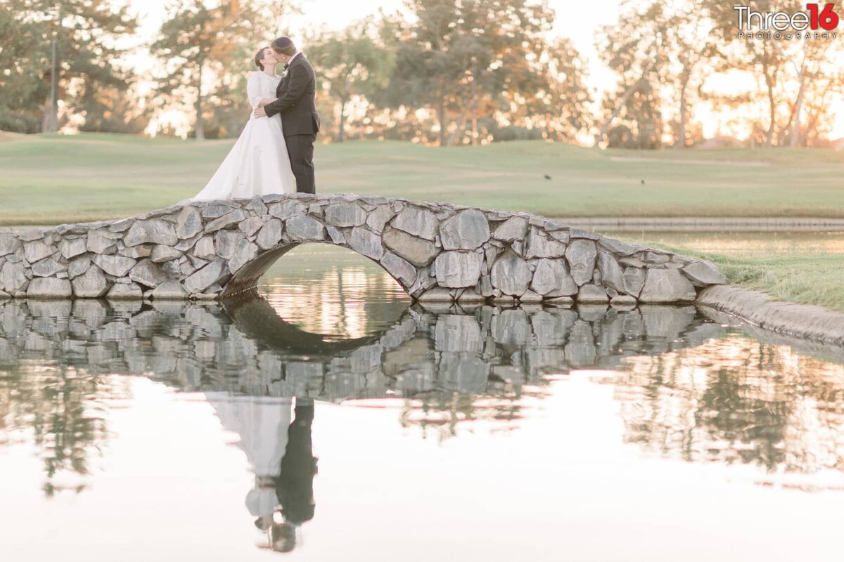 Bride and Groom share a tender kiss while standing on a bridge overlooking golf course lake
