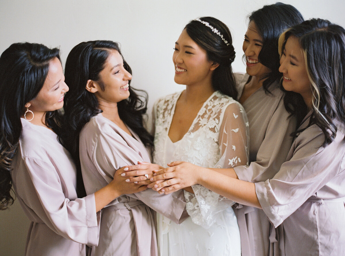 Bride surrounded by bridesmaids in neutral robes during a joyful getting ready moment at Castle Ladyhawke.