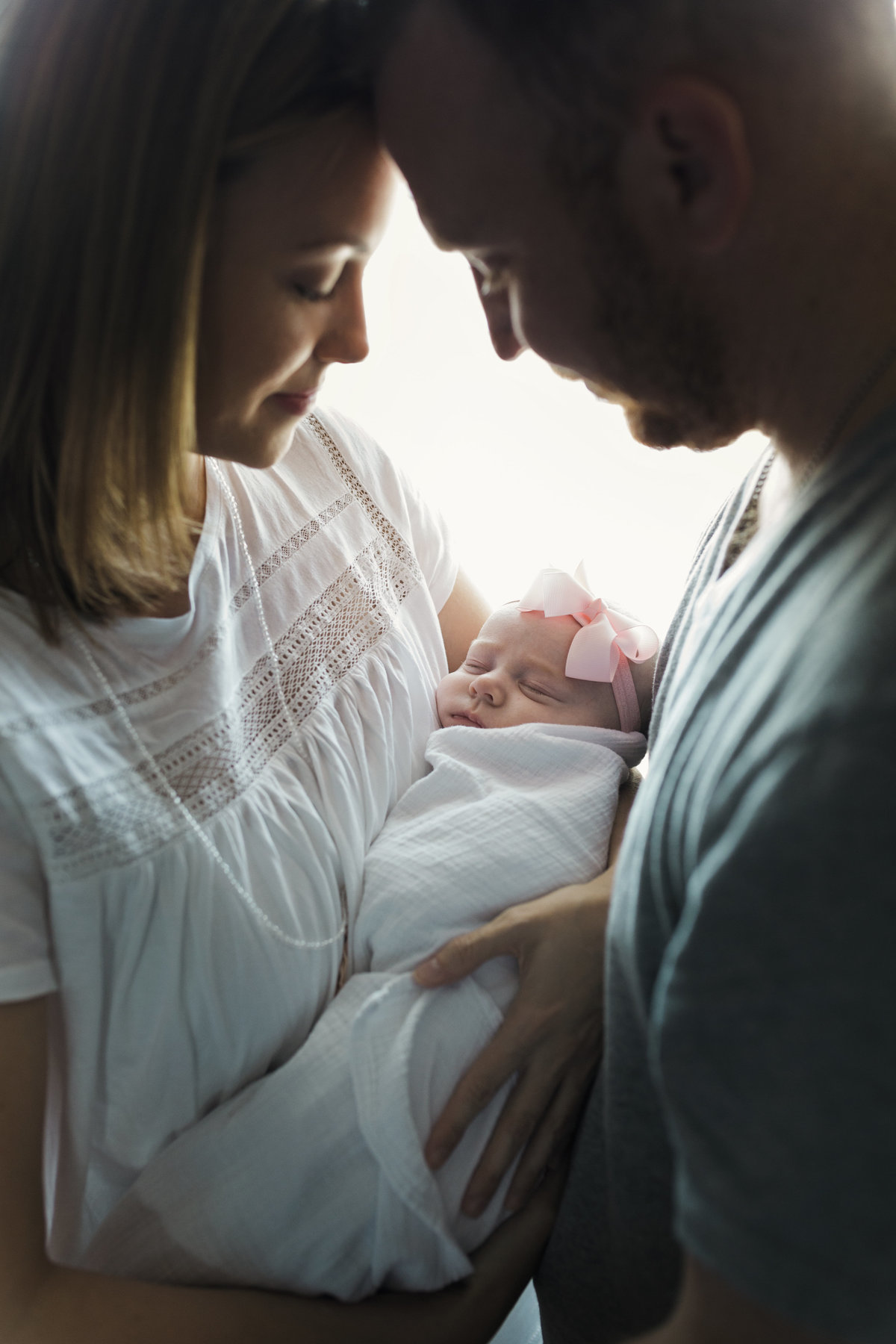 charlotte family photographer creates a beautiful lifestyle image of mother and father embracing their newborn near a window