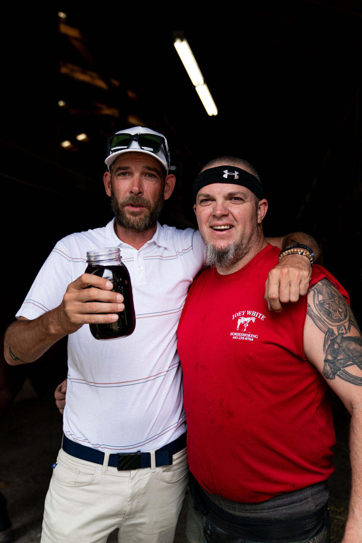 Two men half-hugging while one holds a mason jar full of moonshine at Pinehurst Racetrack in May 2020. Matt Cardis Golf in Your State and Joey White.