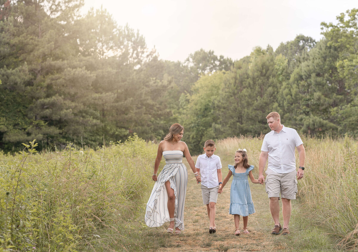 family of  four walking on a field holding hands and smiling