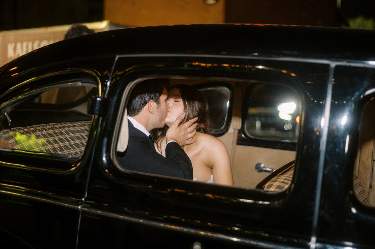 bride and groom kissing in getaway car