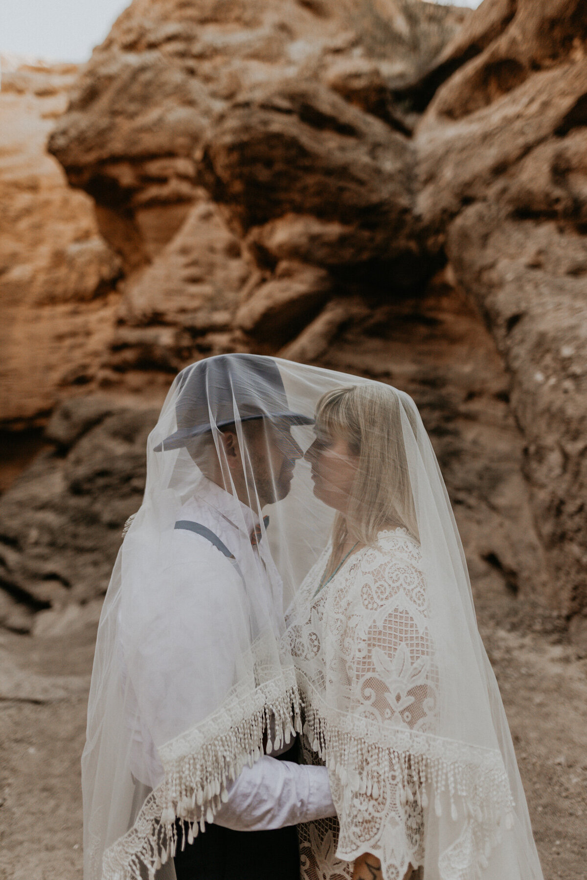 bride and groom standing together vith her veil over their heads