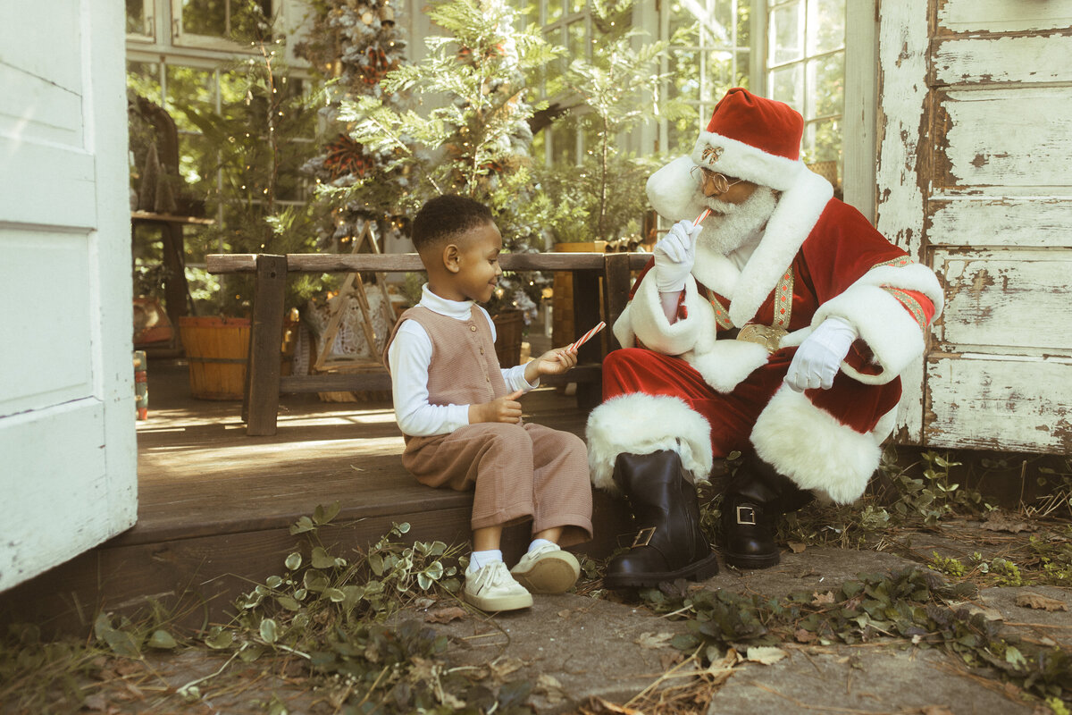 A little boy sits with the Black Santa of Atlanta eating a candy cane at Das Hinterhaus. 