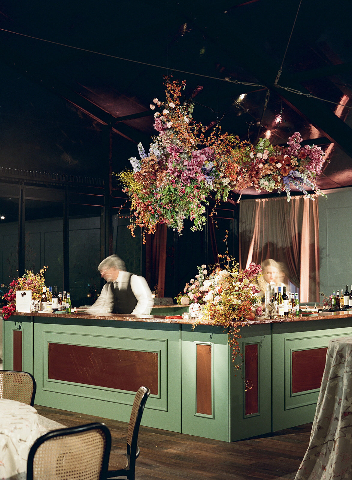 Interacting and sculptural floral clouds hang over the dance floor and bars of this fall wedding reception in Tennessee. Clear top tent build out for fall wedding reception in Tennessee hills.  Product clustered floral clouds in a tasteful fall color palette of copper, ruby, gold, burgundy, rust, and lavender. Orchids, bittersweet berries, butterfly ranunculus, and tulips are highlighted. Unique floral design with flower forward large scale installations. Design by Rosemary & Finch Floral Design in Nashville, TN.