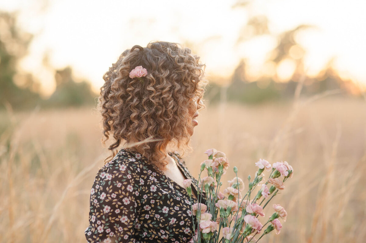 Stunning image of a senior girl at sunset in a tall grass field holding pink florals