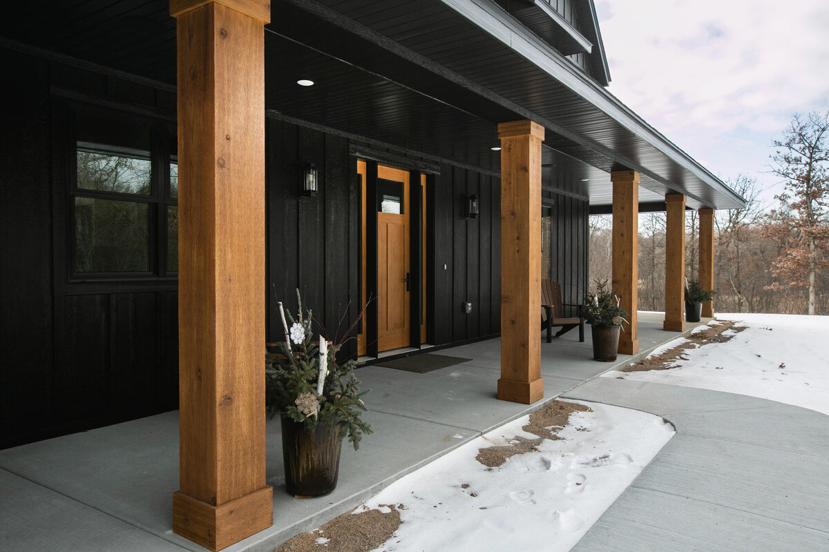 Exterior view of custom home in Elk River, Minnesota with black siding, wood details and front porch built by Cornerstone Custom Builds