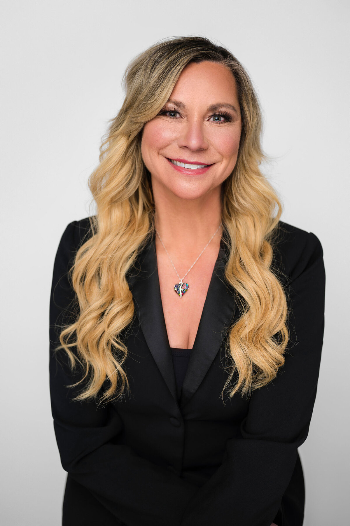 Smiling woman in a black blazer, wearing a heart-shaped pendant necklace