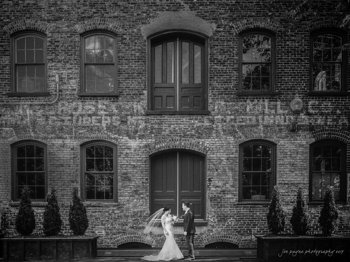 A bride and groom standing outside a brick building admiring each other.