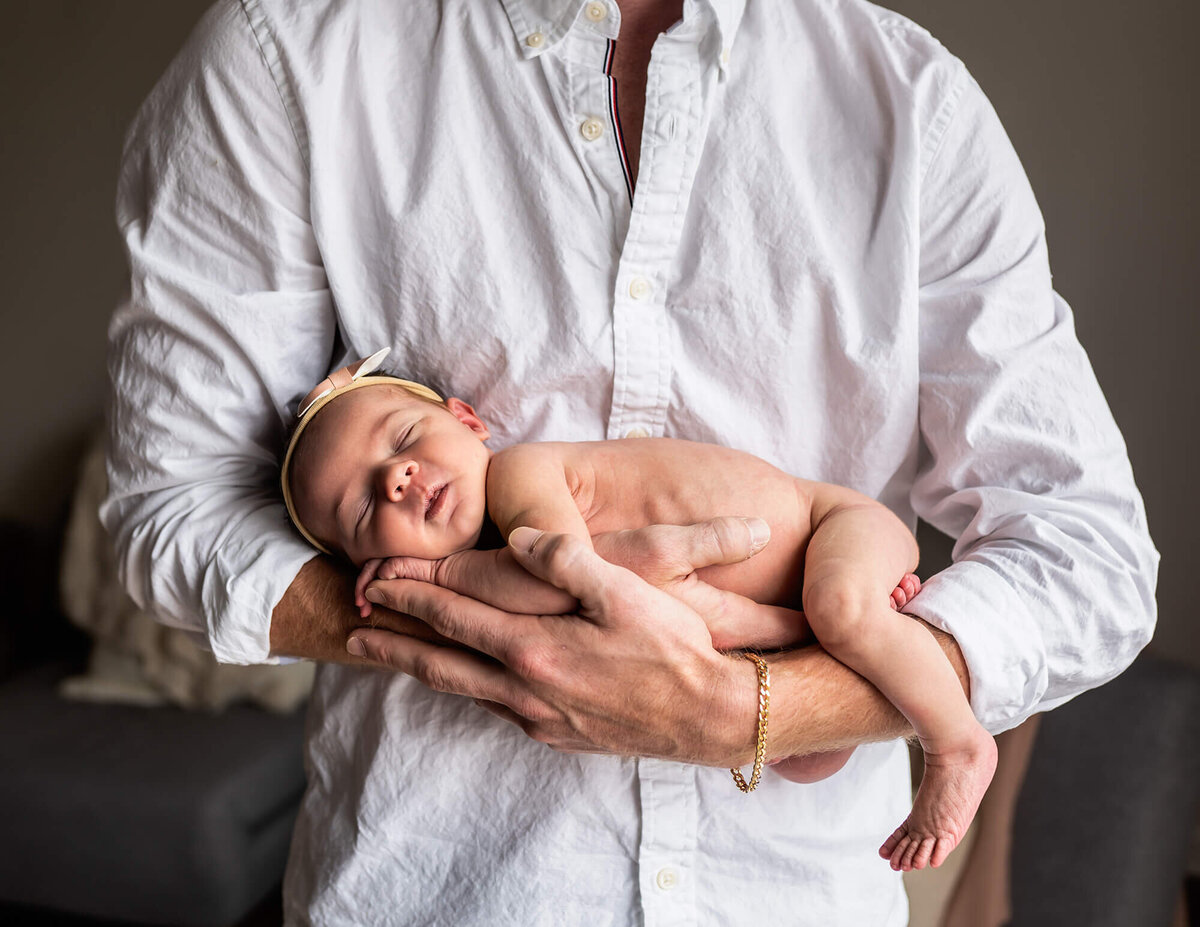 A newborn baby girl sleeps on her tummy while cradles in her daddy's arms