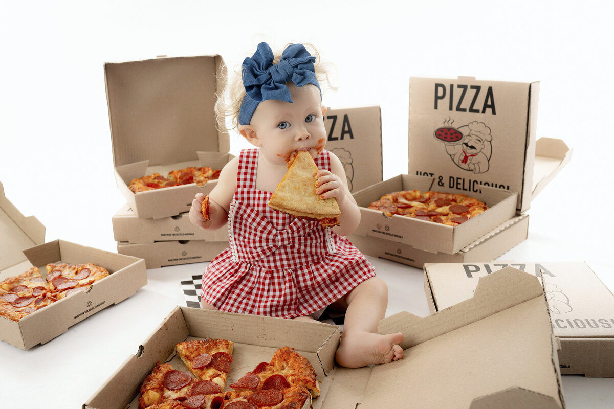 Child in red gingham dress with pizza slices and open boxes around takes Iowa Milestone Photos
