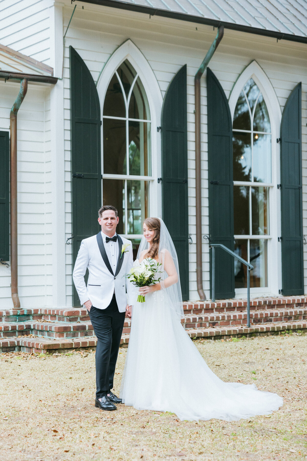 Bride and groom stand outside the arched-window chapel at Palmetto Bluff, Bluffton—captured by luxury wedding photographer Amia Marcell.