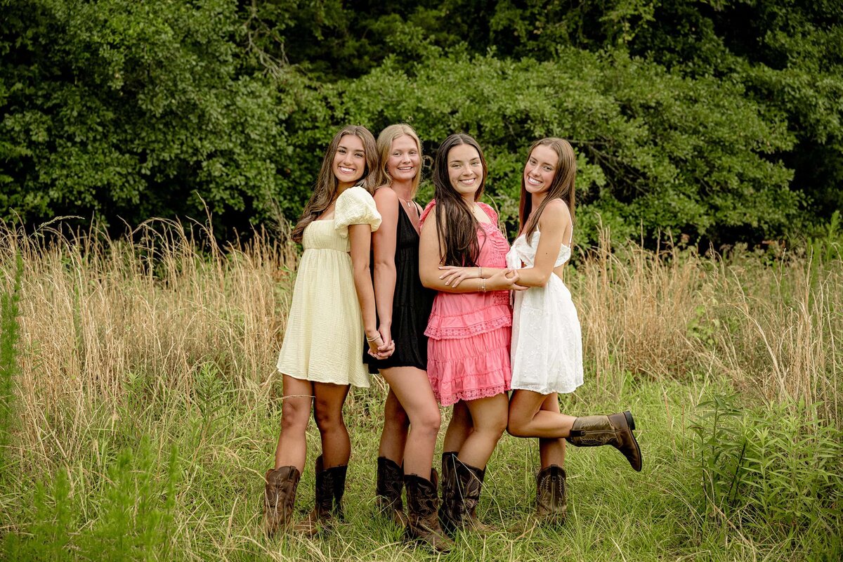 senior best friends laugh and embrace each wearing a sundress as they celebrate in the tall grasses of a field for their best friend senior session