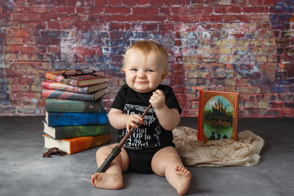 Professional portrait of a nine month old baby posed on a brick background with books