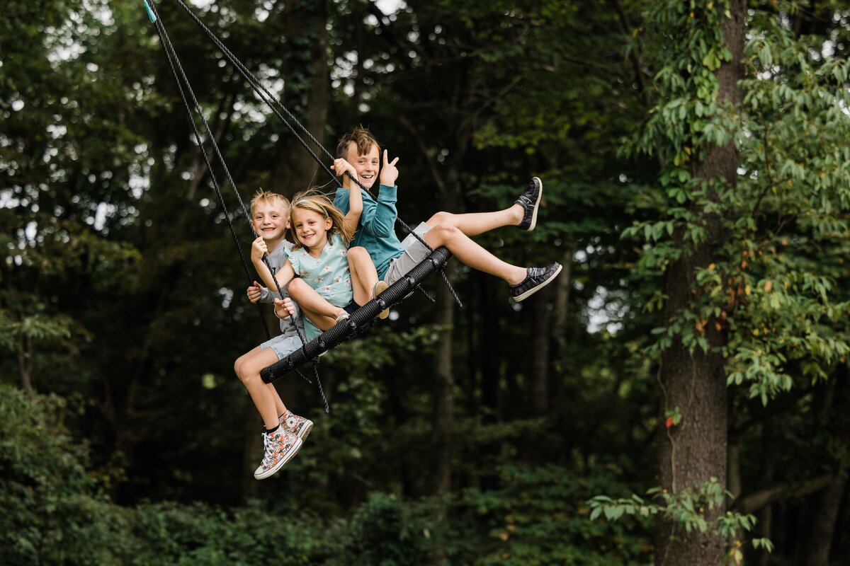 Three children, captured by a talented family photographer from Pittsburgh PA, enjoying a ride on a large swing outdoors.