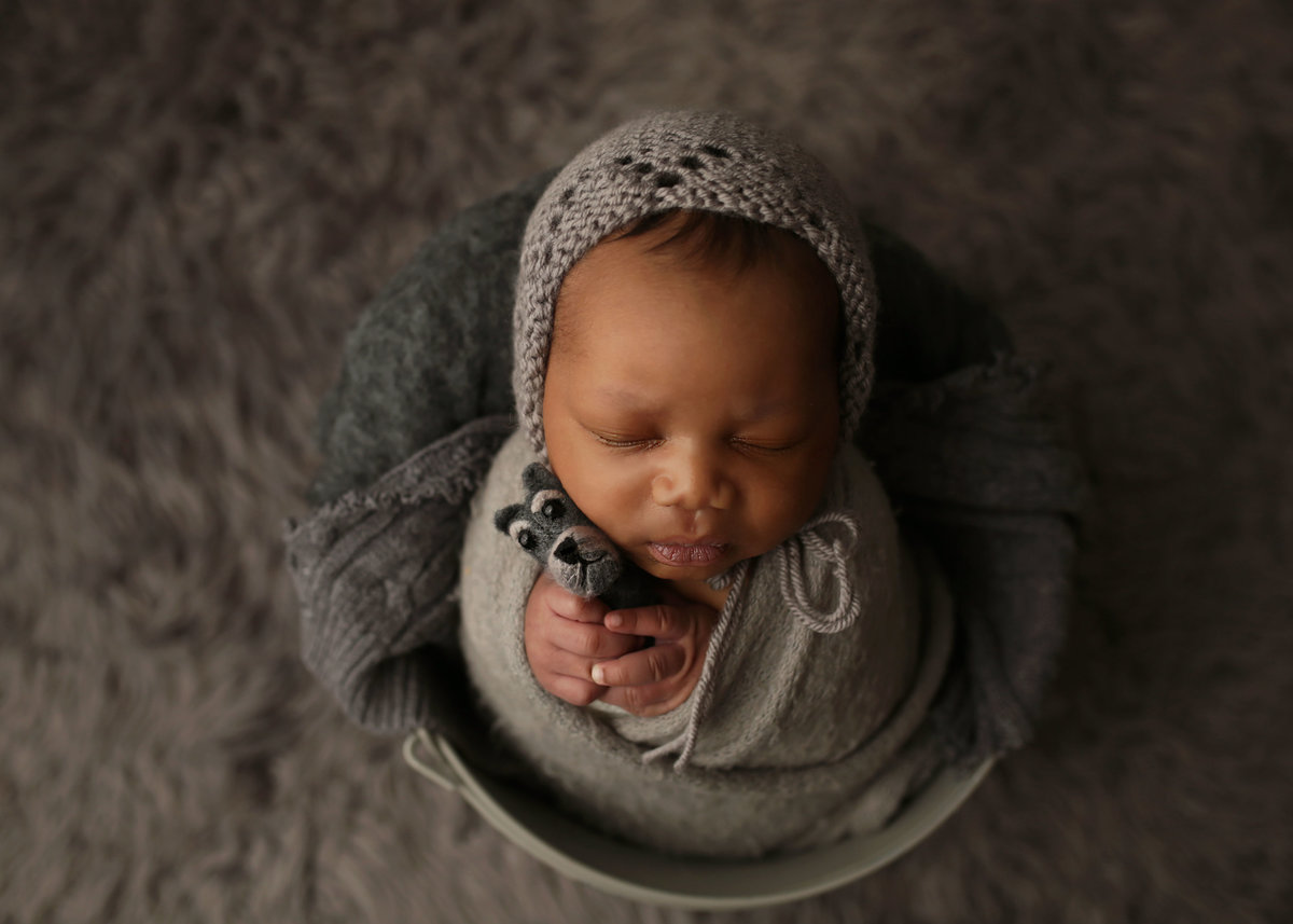 newborn baby wrapped in gray cloth posed in antique bucket on gray fur rug