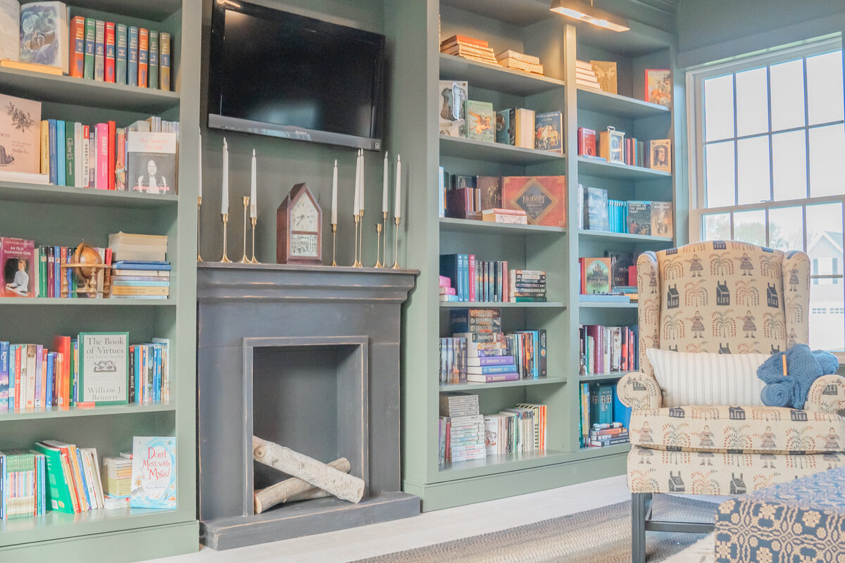 Built-ins for library shelves filled with books and artwork along with faux fireplace and birch logs