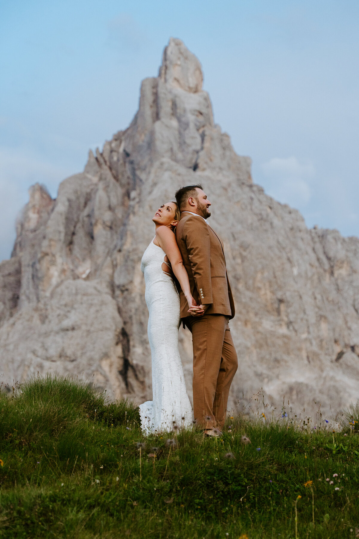Bride and groom standing together under tall mountain cliff