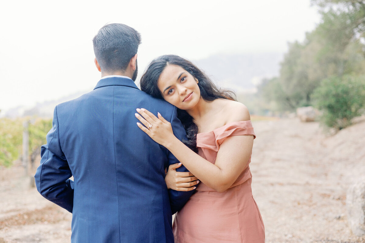 proposal pictures with woman holding her grooms shoulder and facing the opposite direction of him and smiling gently while holding her hand up to his back to show off his engagement ring captured by bay area photographers