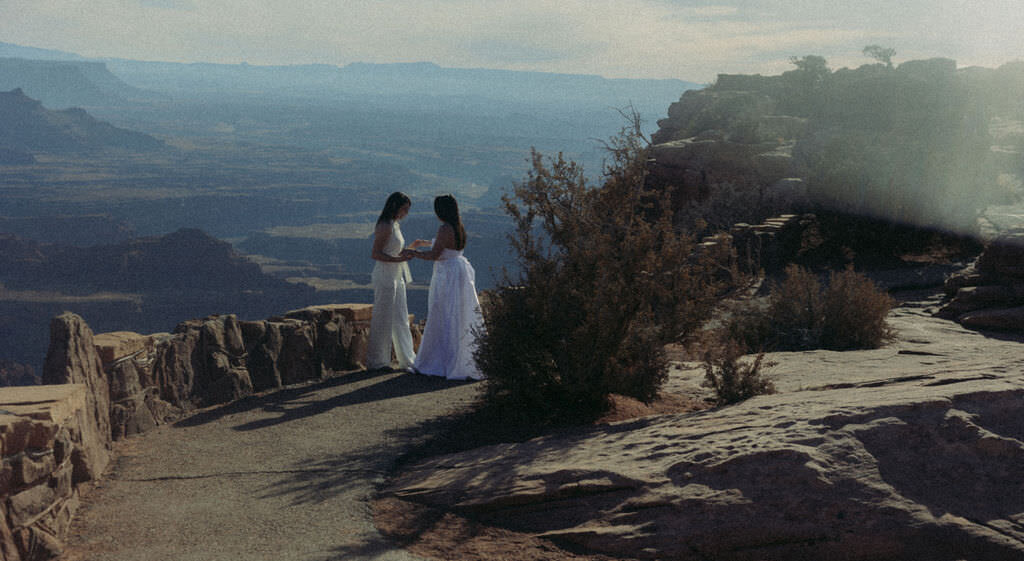 A wedding couple holding hands and standing on a hiking trail.