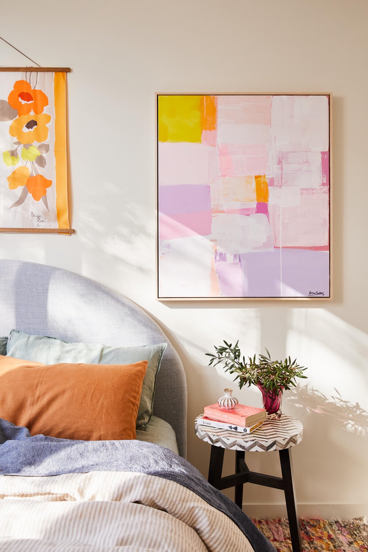 Close-up of pastel and floral artwork above bed with orange cushions in Elwood apartment