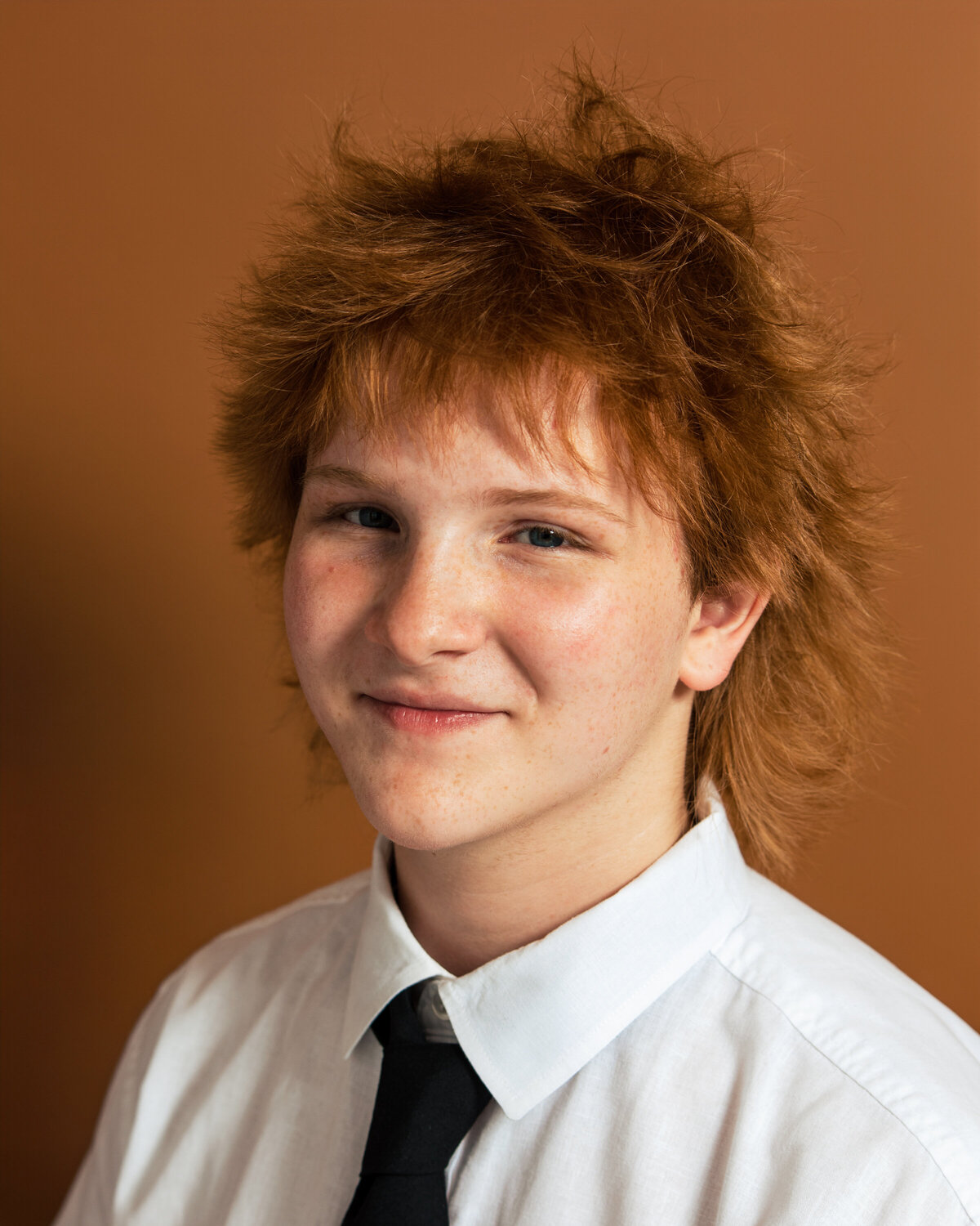 A portrait of a teenage boy taken against a brown background that was used for Theater headshot