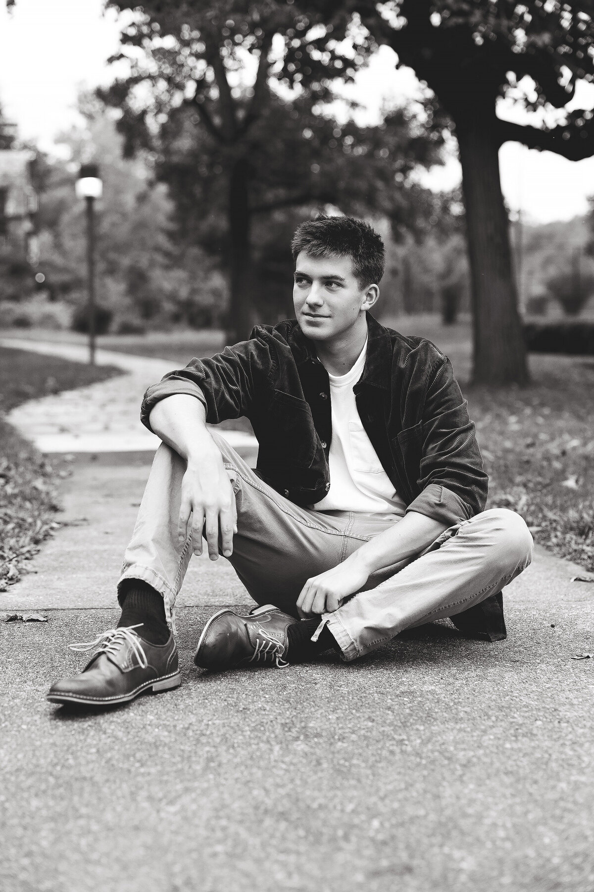 Boy sits on walk way looking away from camera for high school senior portraits in Greensburg.