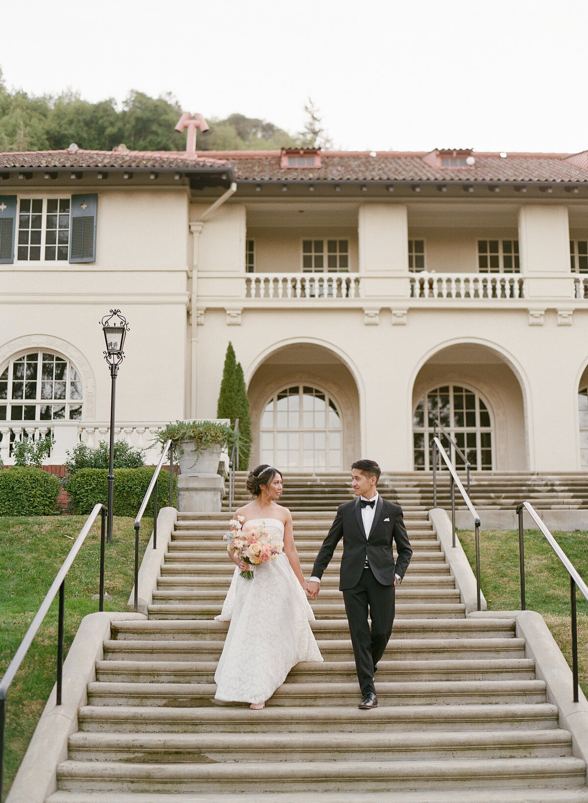 A romantic moment of a bride and groom walking hand in hand down the elegant venue stairs at the Montalvo Arts Center on their wedding day. The stunning architecture and lush surroundings create a timeless and sophisticated backdrop for this special occasion