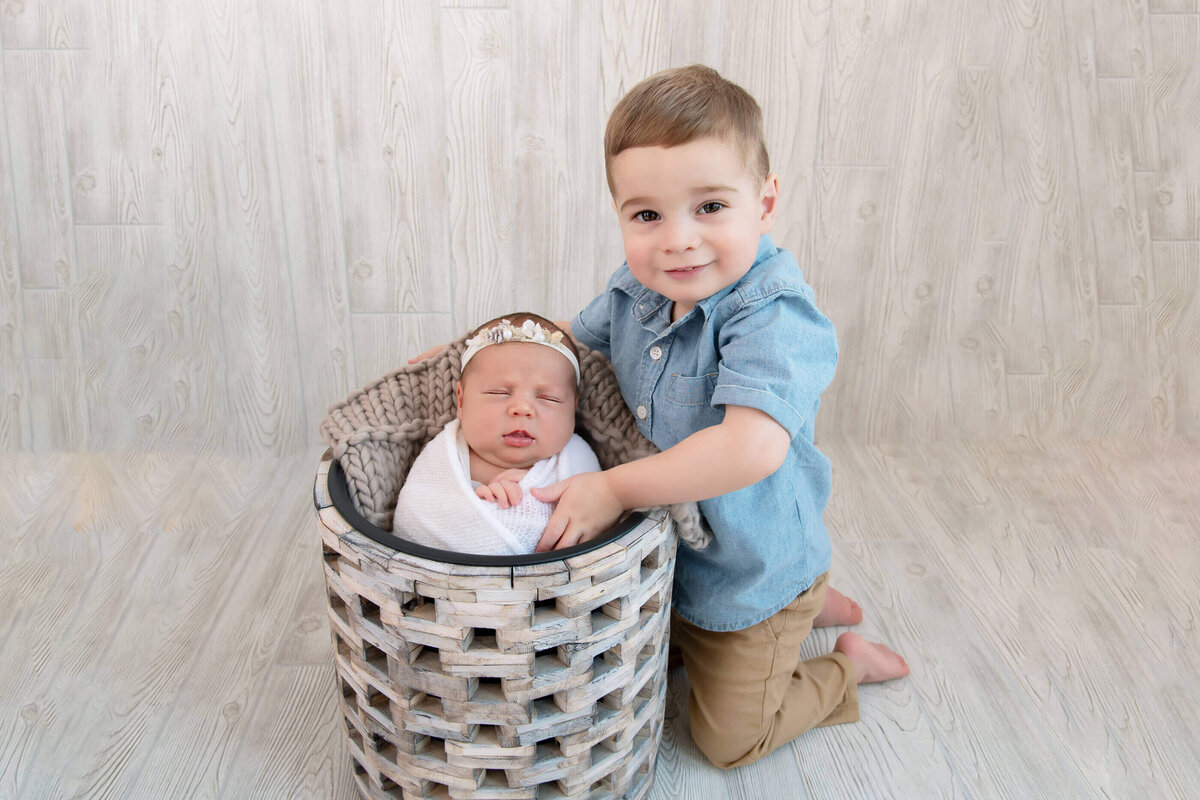 Boy toddler with his newborn sister in a buck for their newborn photography session