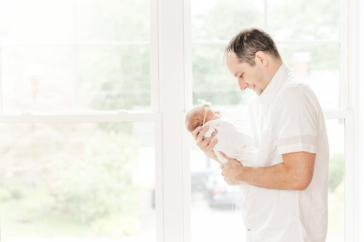 Dad holds baby by window during in home newborn photo session with Sara Sniderman Photography in Natick Massachusetts