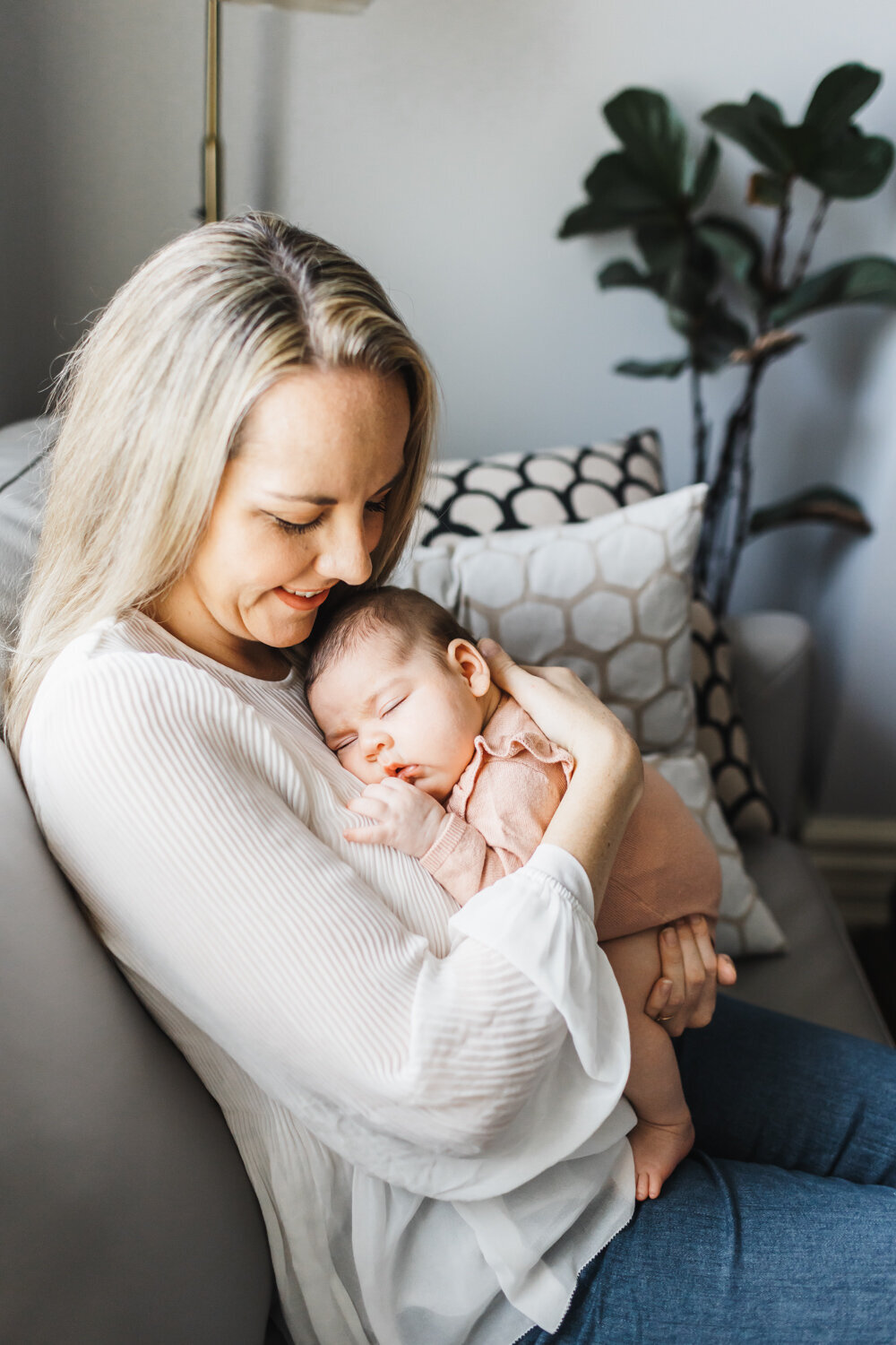 Stylish first time mom snuggling her sleeping newborn daughter on the couch in  her Toronto home