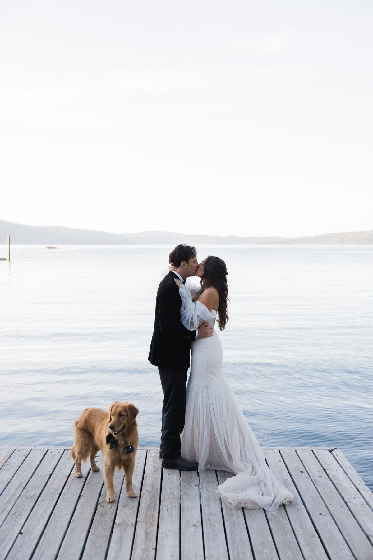 Bride and groom kissing on a jetty with a dog at Idaho lakeside wedding