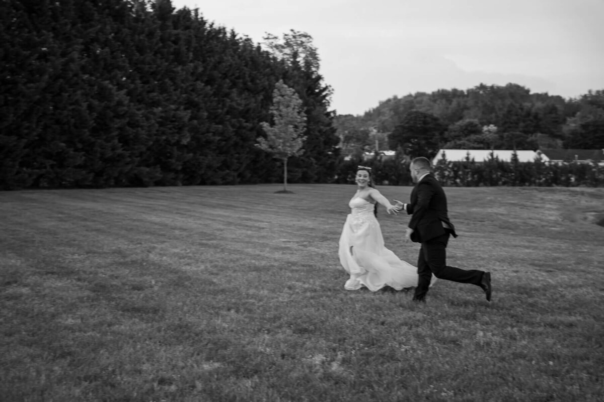 Bride & Groom gracefully jogging through a field hand in hand while lovingly gazing at each other