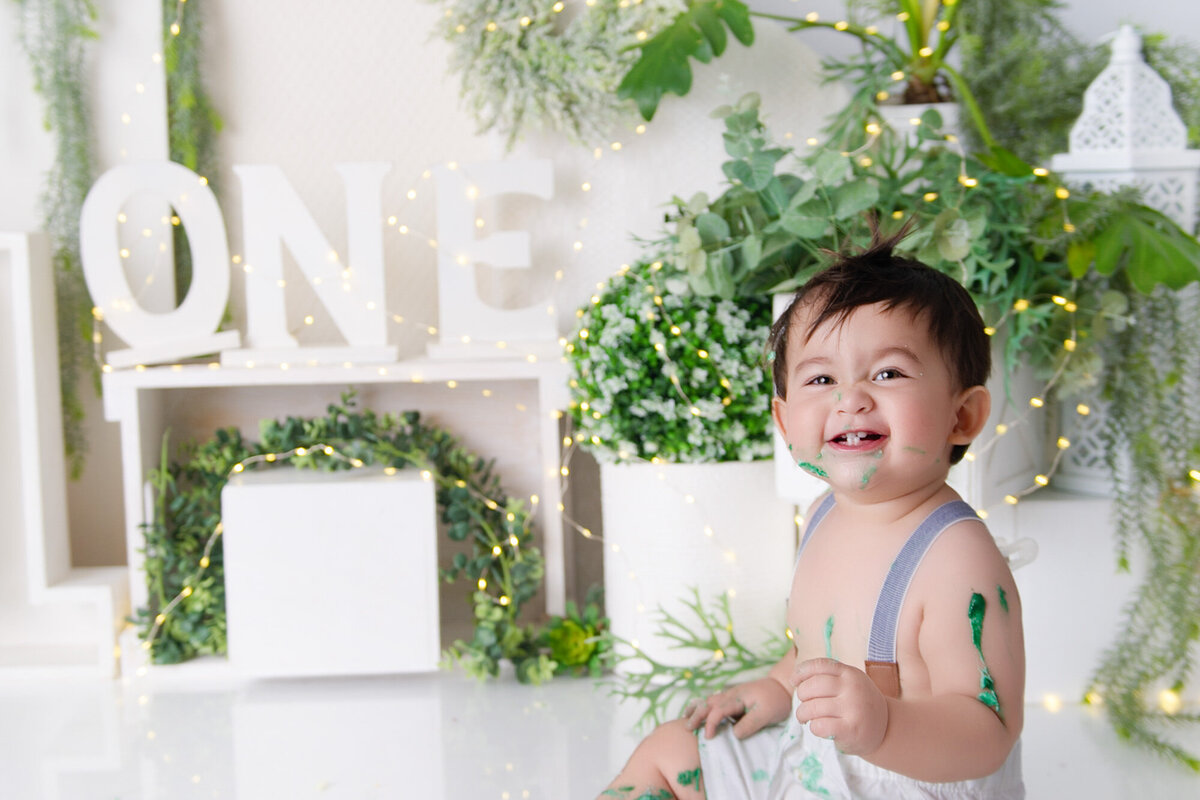 greenery white backdrop one year old baby on bike cake smash