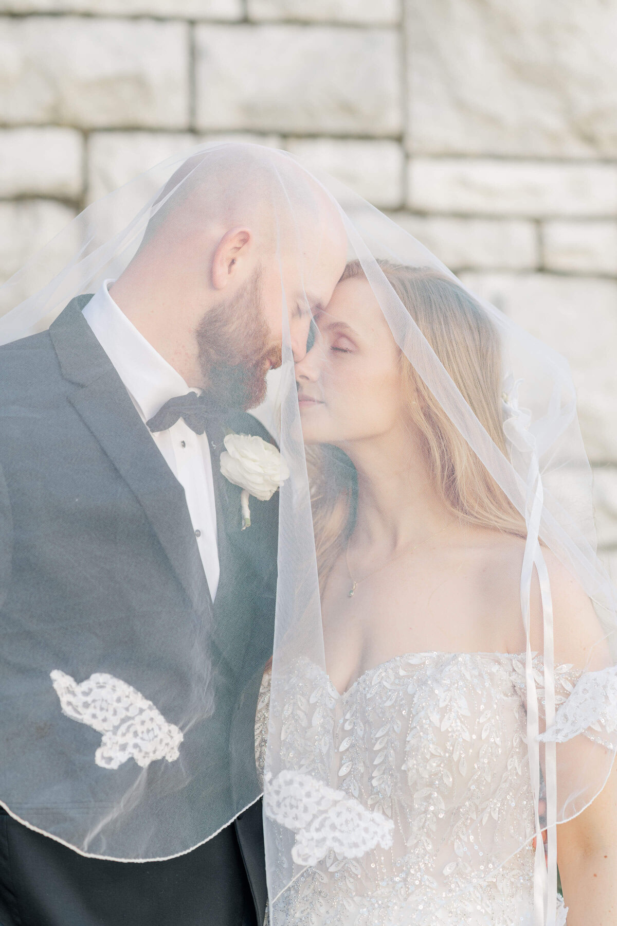 Bride and groom under veil  looking towards each other with eyes closed