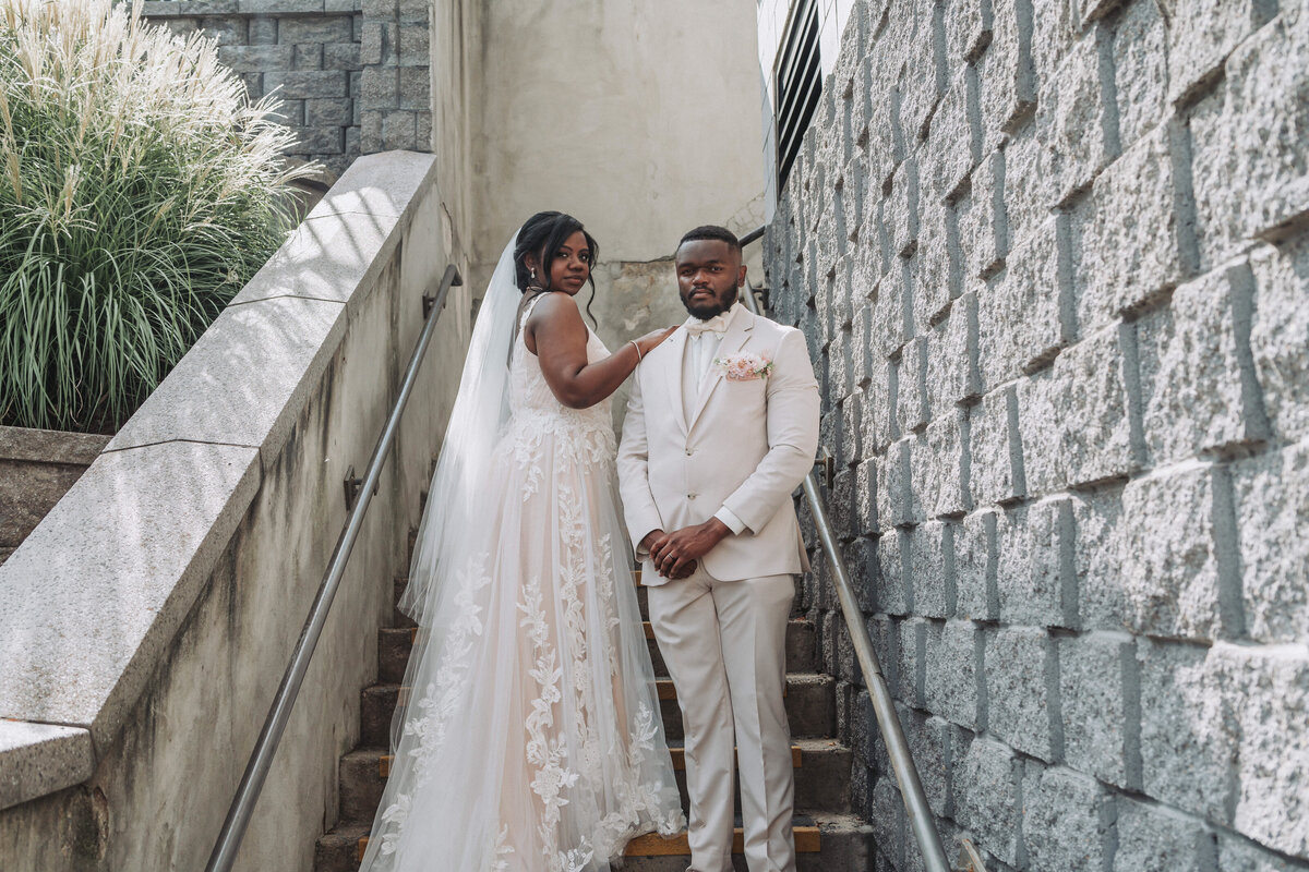A beautiful wedding couple poses lovingly on a textured stone staircase, with the bride looking back at the camera, at the Massanutten Conference Center and Resort in Massanutten, Virginia, captured by Quinn Photography LLC.