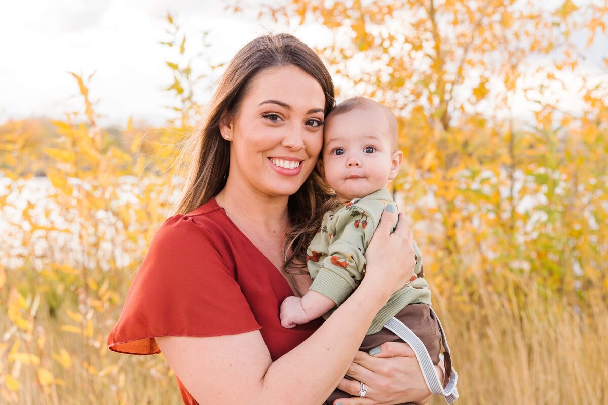 mom and baby snuggle with fall leaves at Golden Ponds