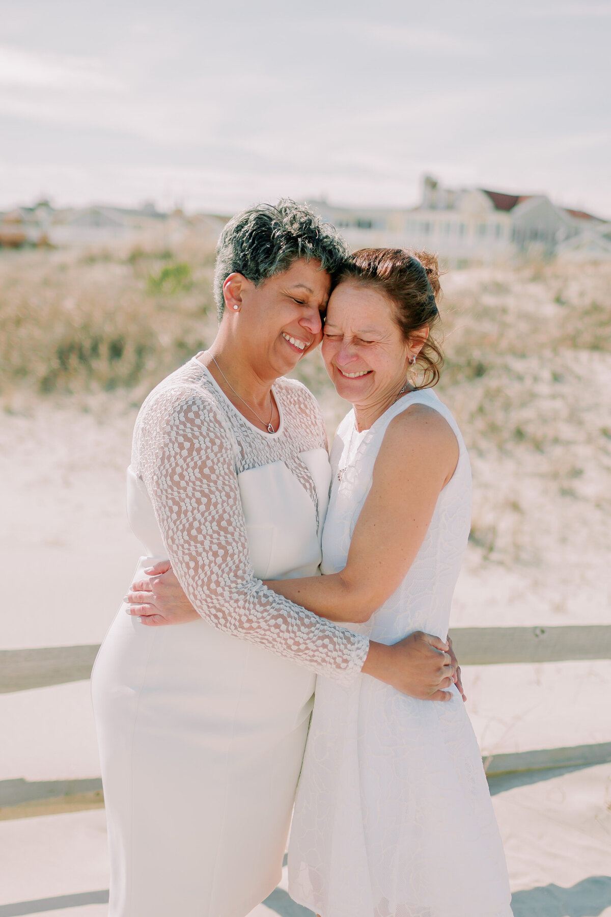 A newlywed couple in wedding dresses hugging and laughing 