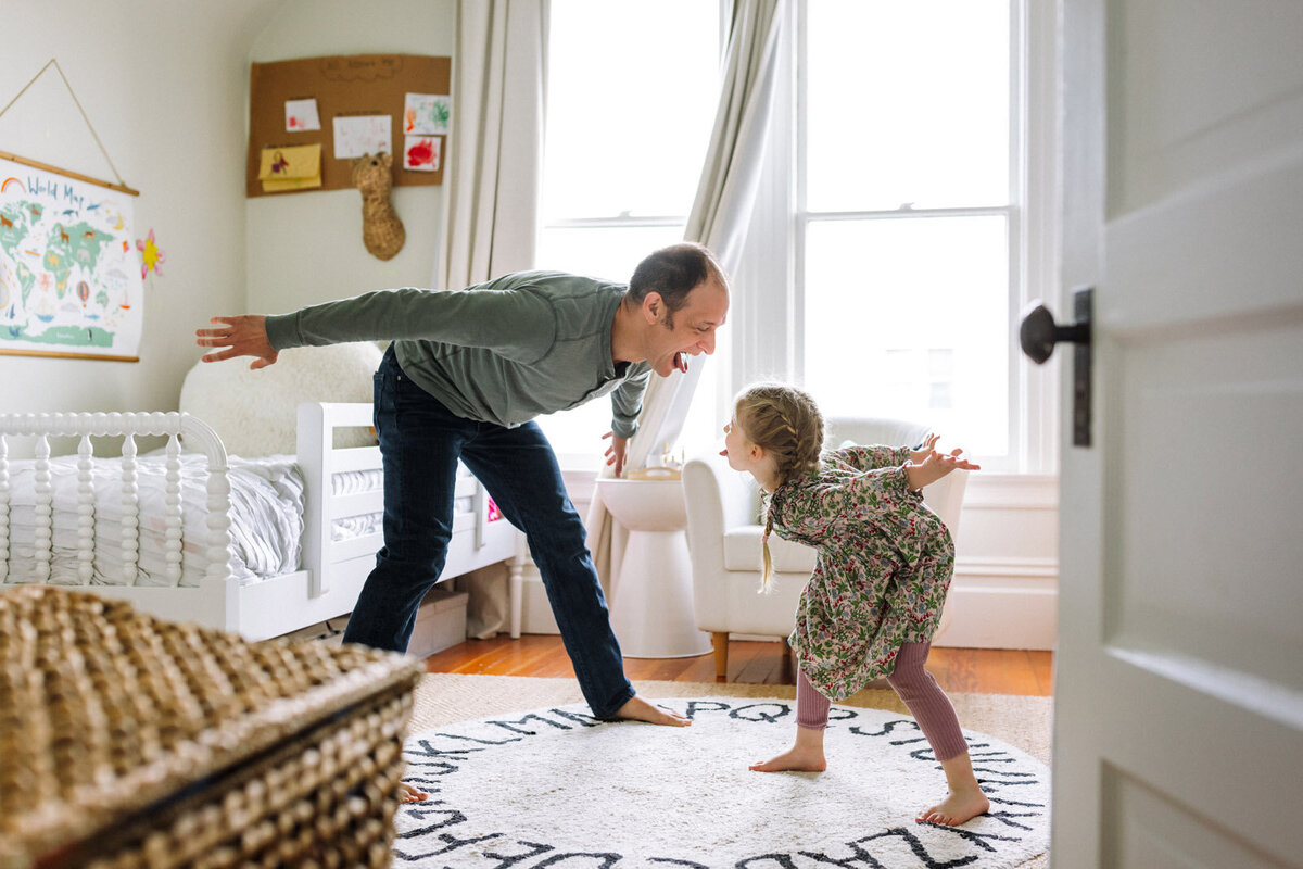 dad and daughter both leaning over towards each other with their tongues out and laughing in girl's bedroom