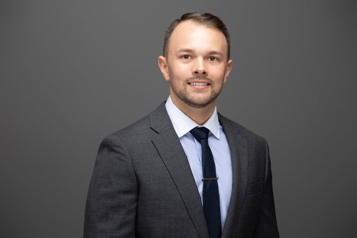 A businessman in a grey suit jacket poses for a professional headshot on a grey background for Janel Lee Photography studios in Cincinnati Ohio