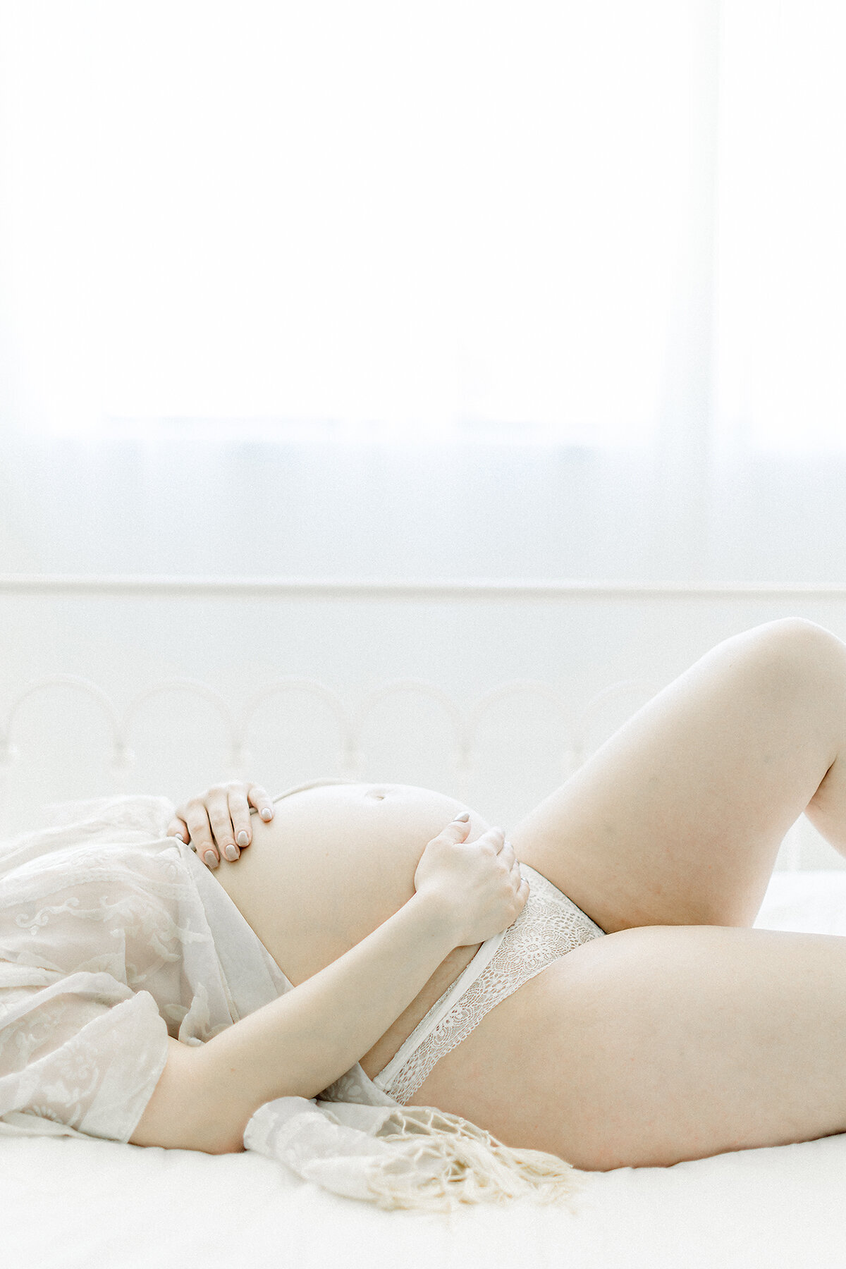 A side profile of an expecting mother laying down in a bed while she is embracing her growing belly as she is being photographed by a Dallas maternity photographer in their studio.