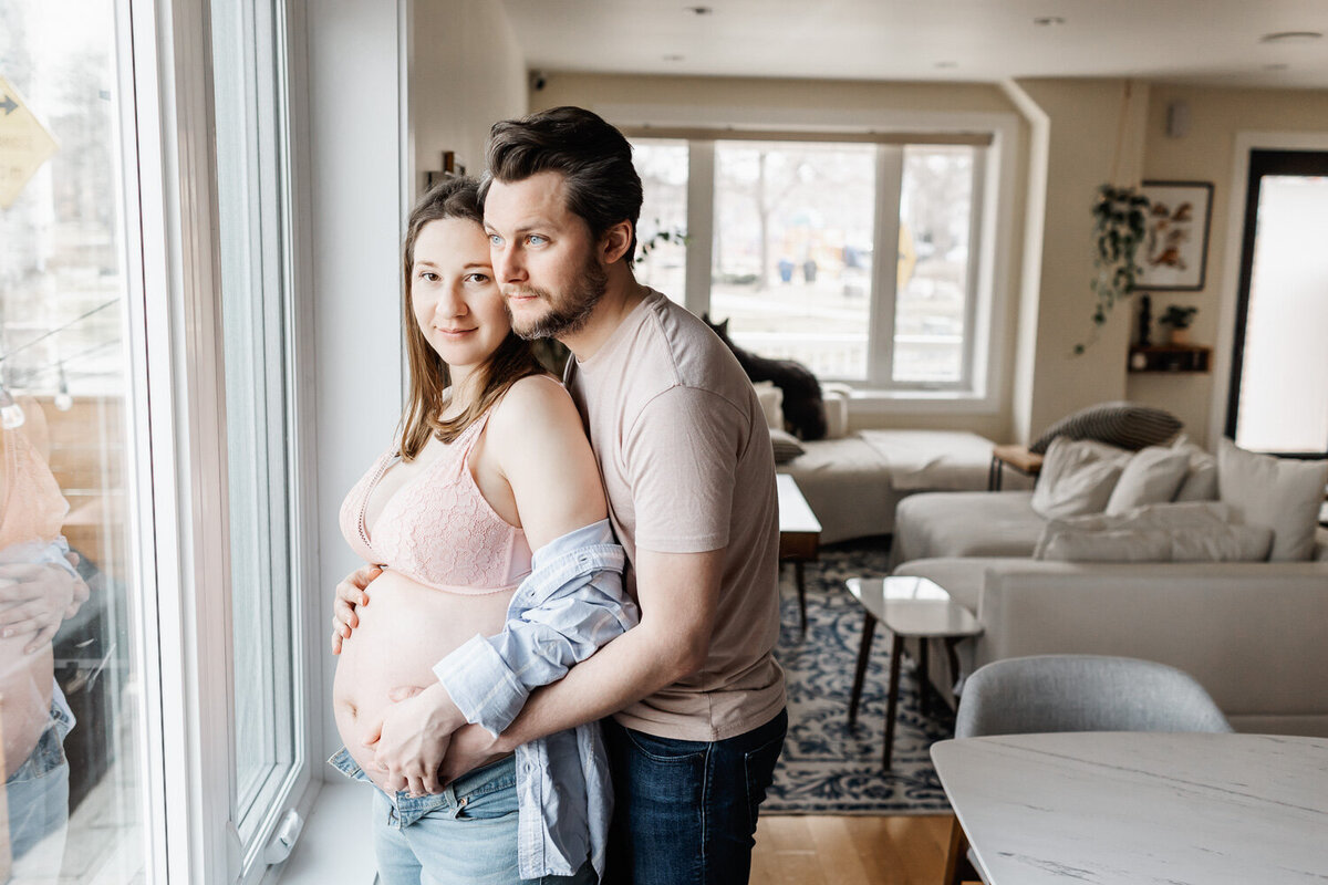 Expecting couple standing next to dining room window