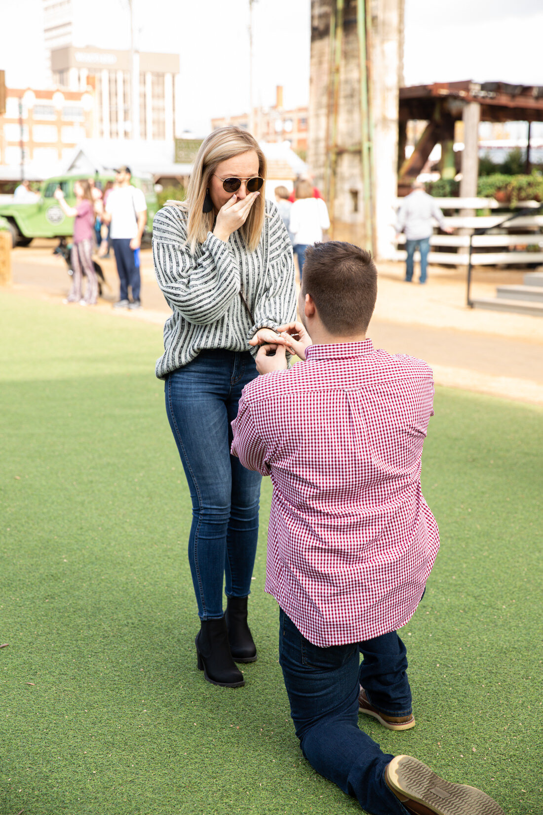A man is kneeling down to propose to a woman on a grassy field, captured beautifully by an Austin wedding photographer.