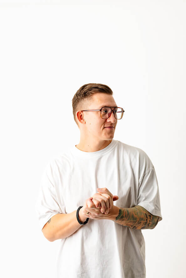Mans clasps hands in white photos studio and looks off to the side.