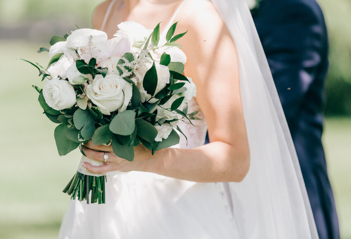 Bride holding luxurious bouquet of white roses and eucalyptus at gorgeous outdoor wedding ceremony