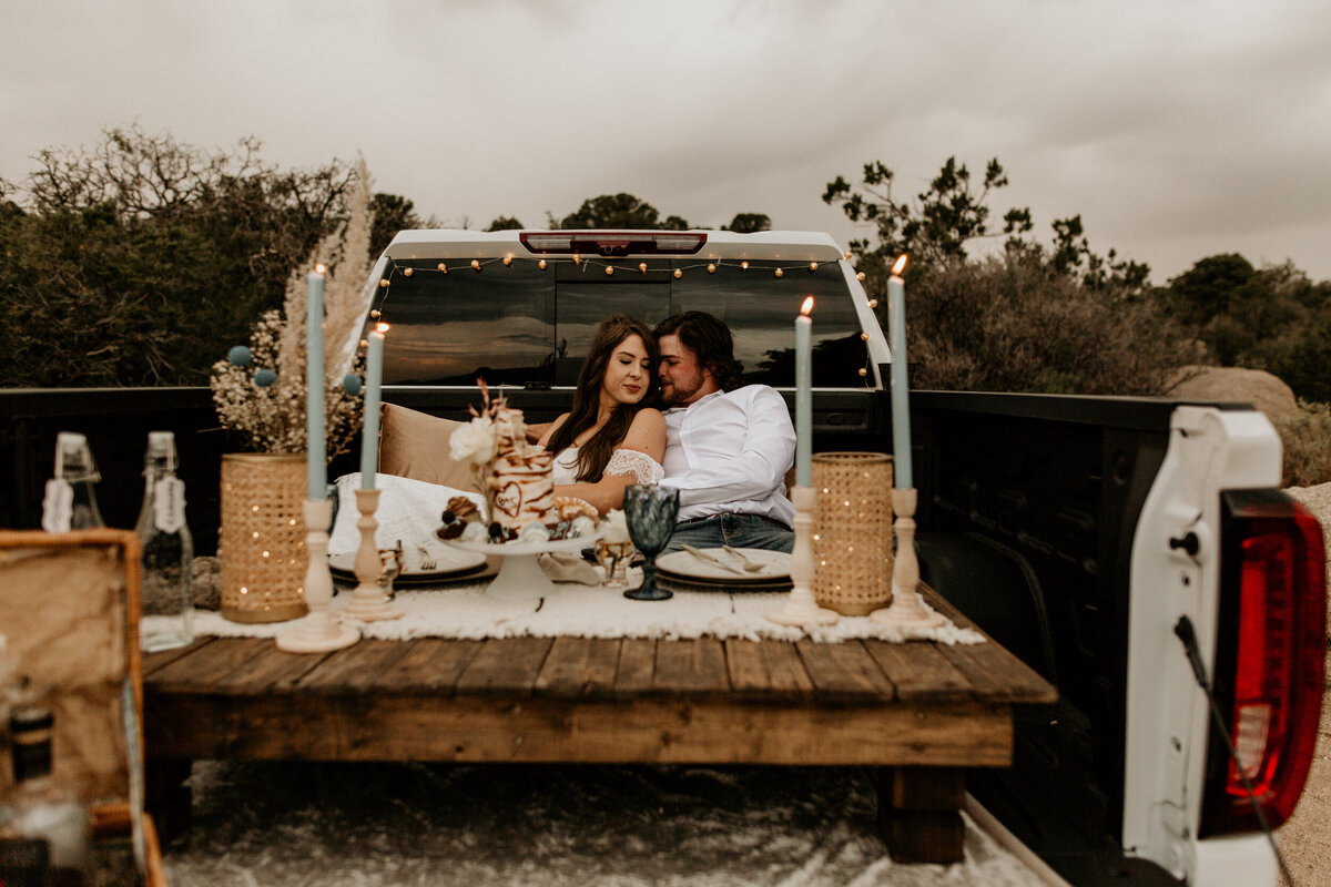 bride and groom eating cake in their truck bed picnic setup