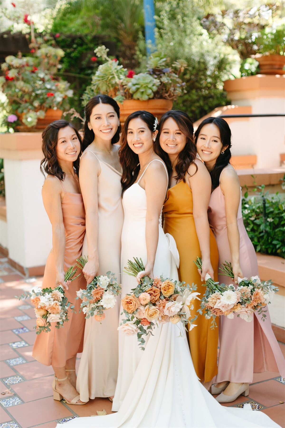 Bridesmaids in gold and peach dresses holding bouquets with the bride